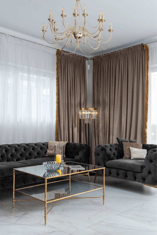 Ein Wohnzimmer mit hoher Decke, braunem Vorhang, Kronleuchter und Stehlampe
