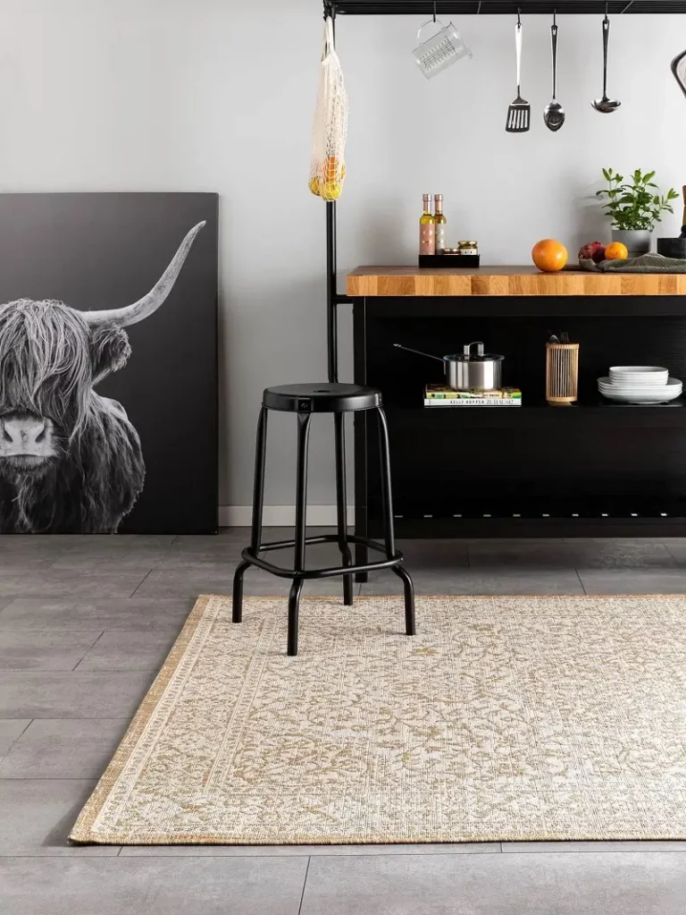 Eine moderne Küchenszene mit einer schwarzen Insel und Hockern, akzentuiert durch ein großes Rinder-Wandbild und einen creme- und beigefarbenen Teppich auf grauem Boden.