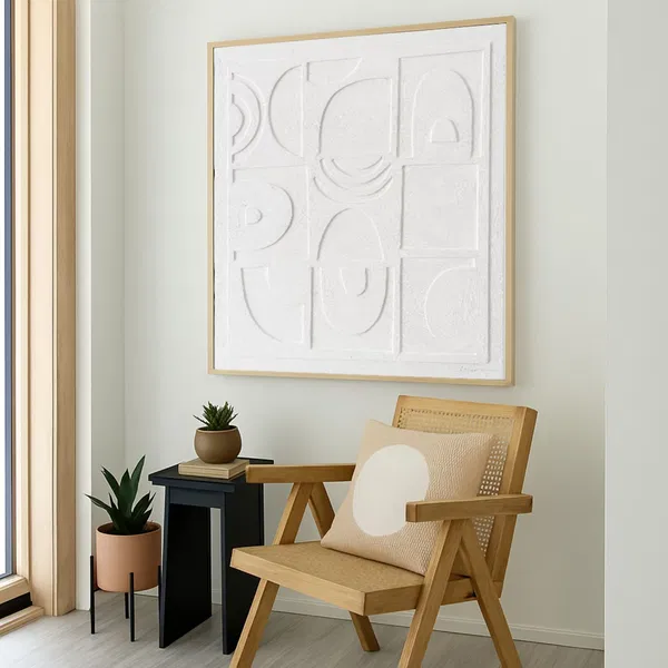 Eine gemütliche Ecke mit einem Holzstuhl und einer kleinen Topfpflanze, über der ein strukturiertes weißes Gemälde in minimalistischem Design hängt.